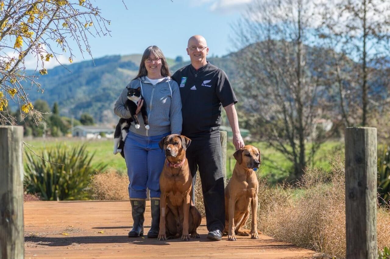 Une famille avec deux chiens se promène sur un chemin de terre, avec des montagnes en arrière-plan.