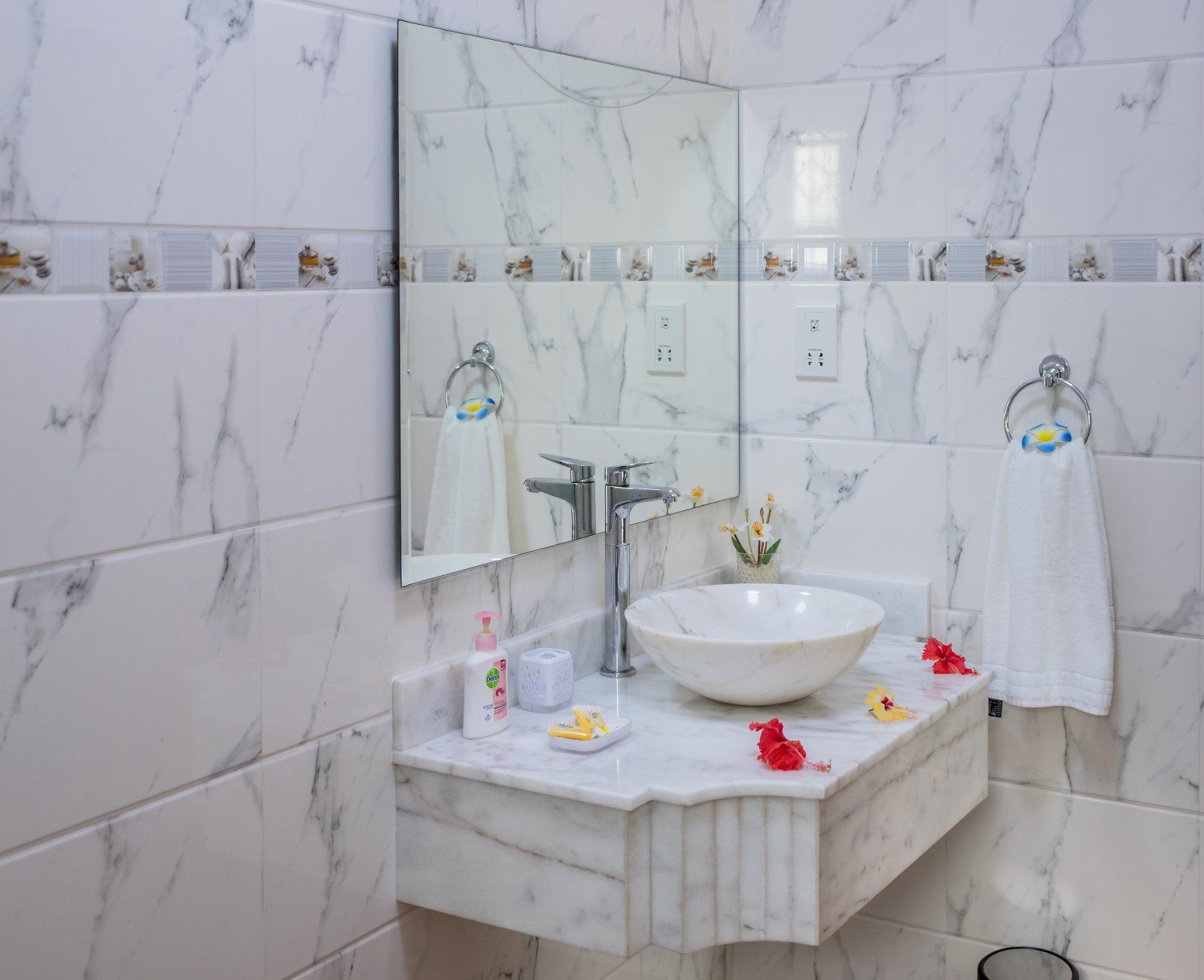 Un baño con lavamanos de mármol blanco, un espejo grande y un aro para toallas.