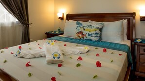 A hotel room with a neatly made bed, floral decorations, and a wooden headboard.