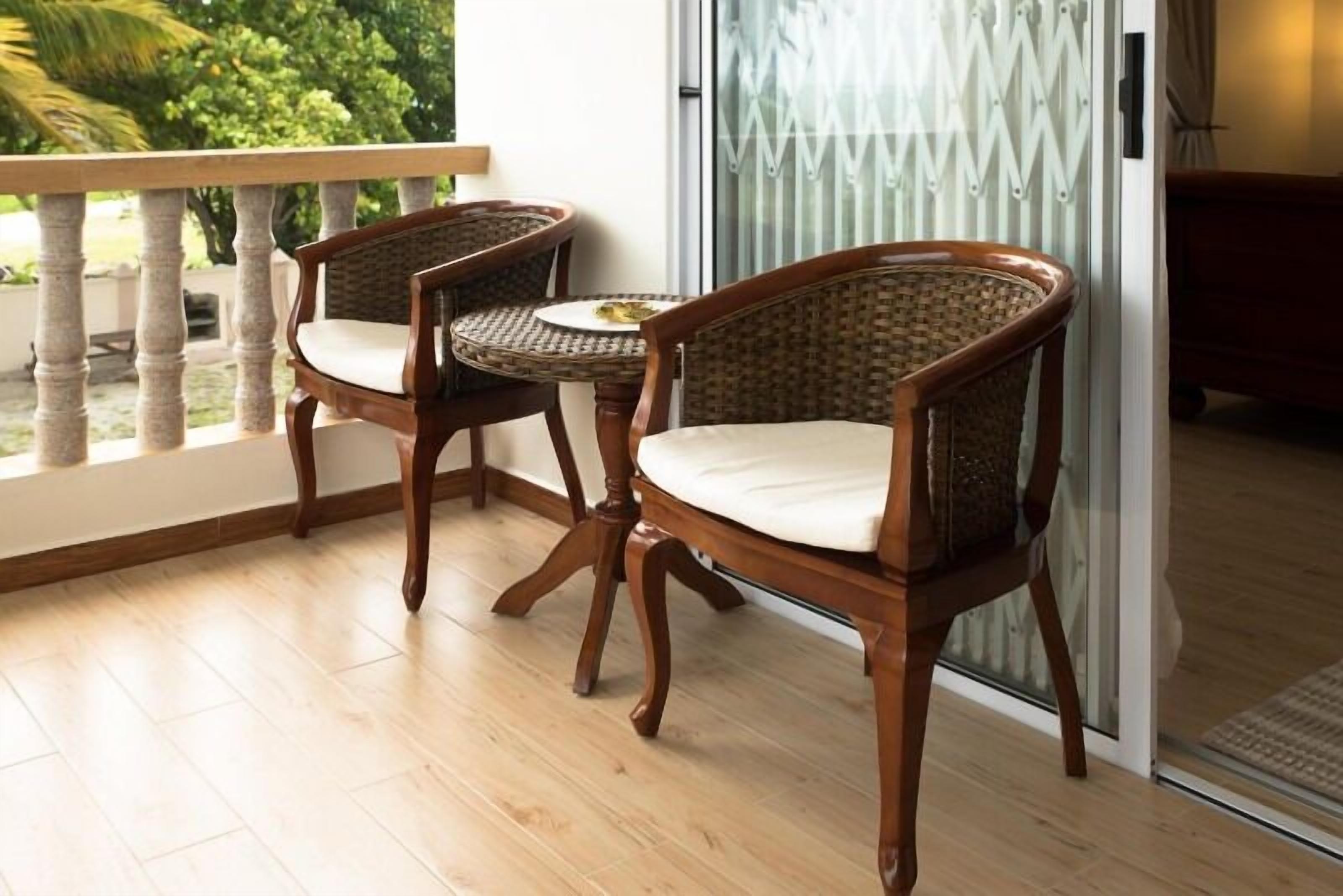 A balcony with two wicker chairs and a small table, a sliding glass door, and a view of greenery.