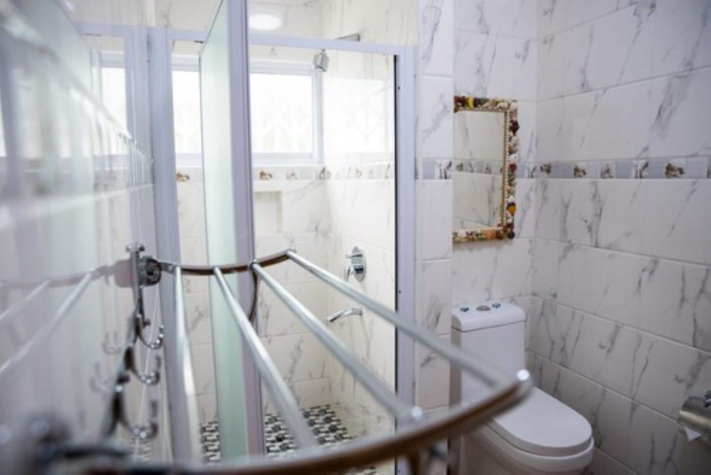 A bathroom with a glass shower enclosure, a toilet, and a marble-tiled wall.