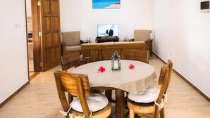 A dining area with a round wooden table, four chairs, a television, and a beach view painting on the wall.