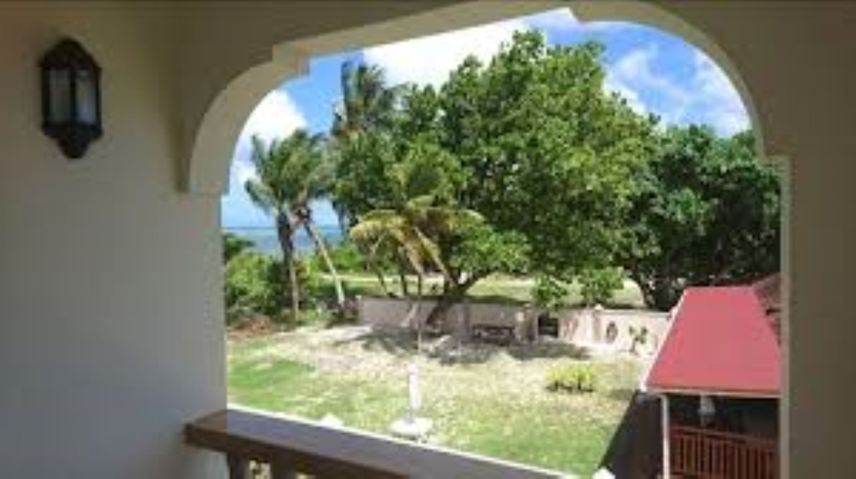 A view from a balcony with a clear sky, palm trees, and a distant view of the ocean.