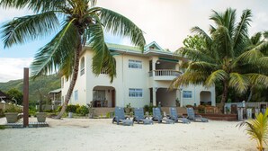 A beachfront property with a two-story building, a balcony, and several lounge chairs on the sand.