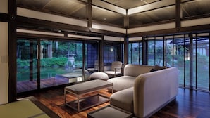 A modern interior with a sofa, chairs, and a view of a garden through large windows. - ryugon (Minamiuonuma)