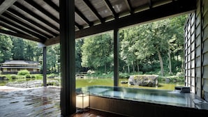 A traditional Japanese-style building with a wooden deck, a hot spring bath, and a view of a pond and forest. - ryugon (Minamiuonuma)