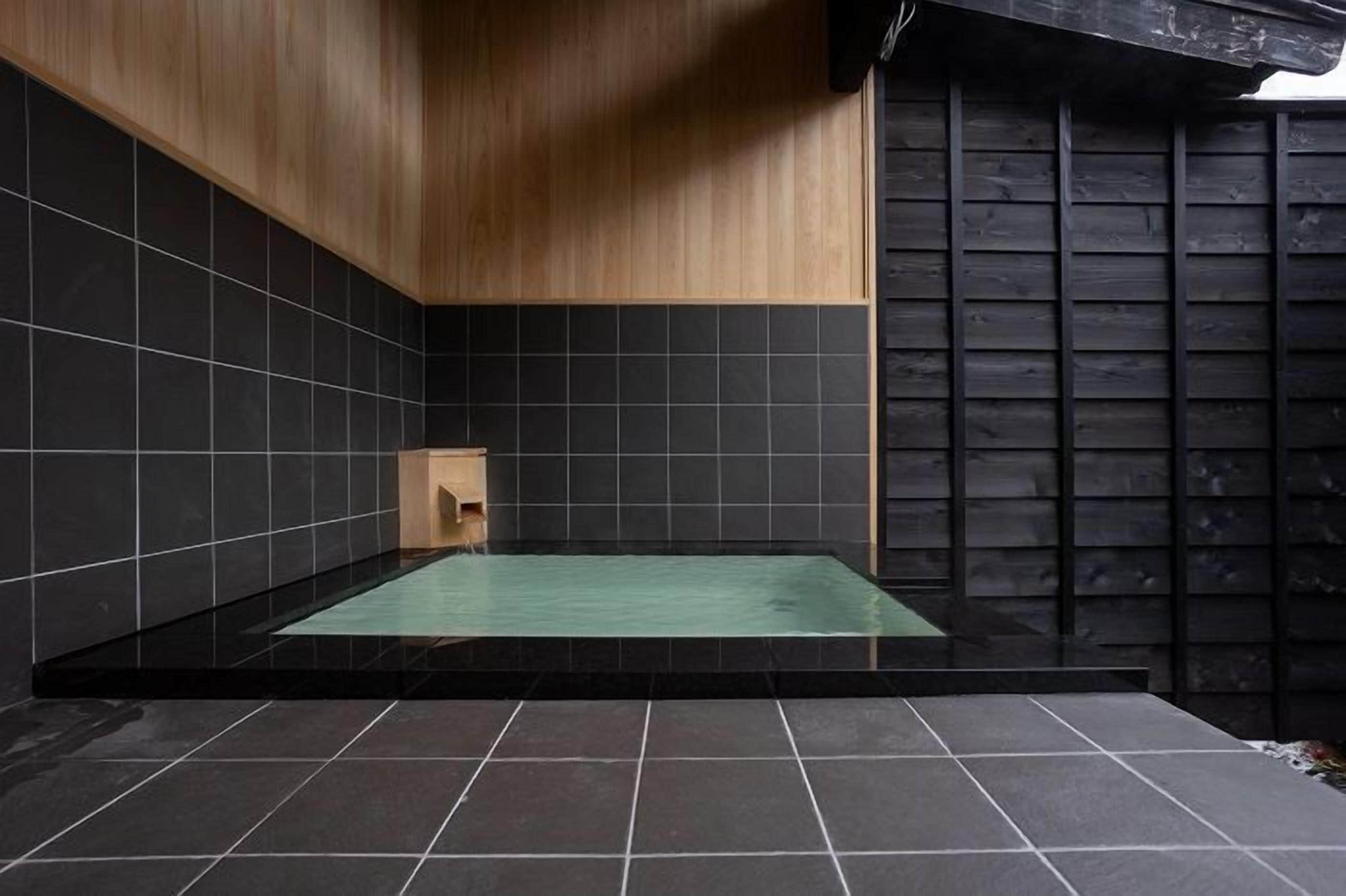 A modern bathroom with a glass-enclosed bathtub, dark tiles, and wooden accents.