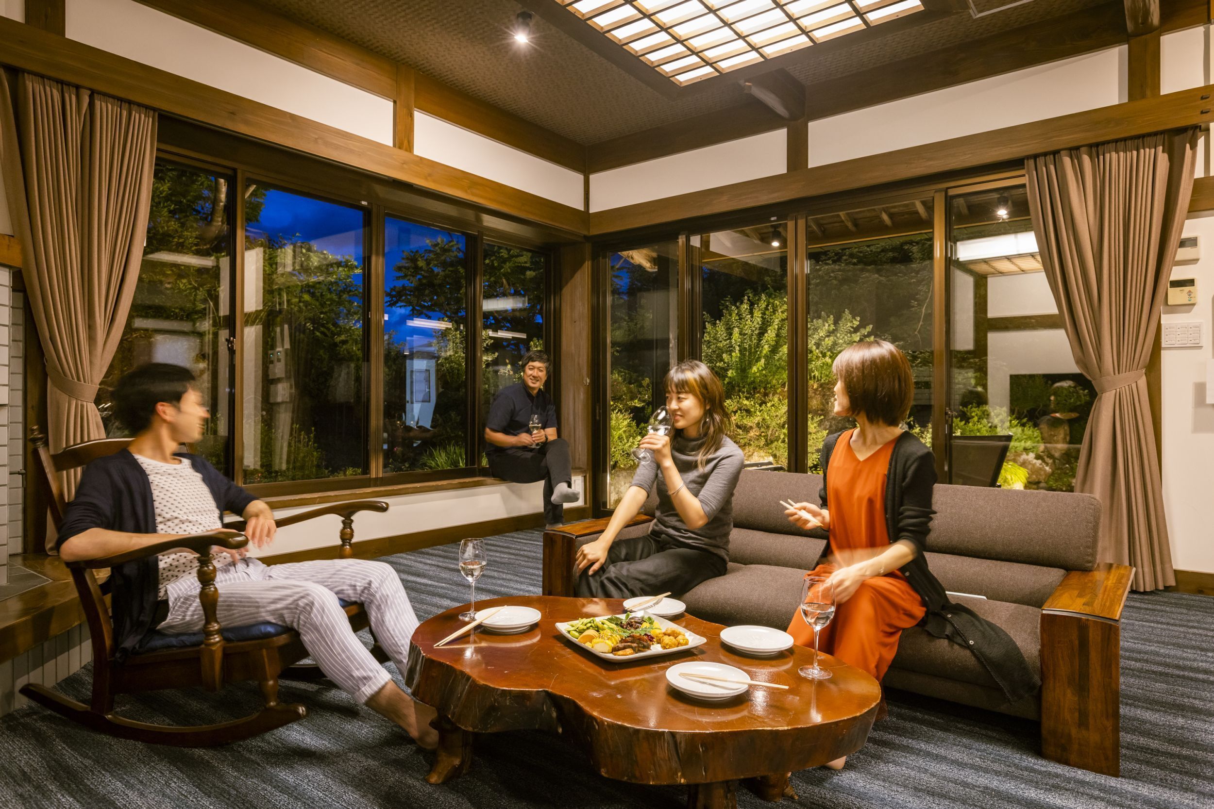 A room with a large window, a wooden rocking chair, a sofa, and a dining table with plates and glasses.