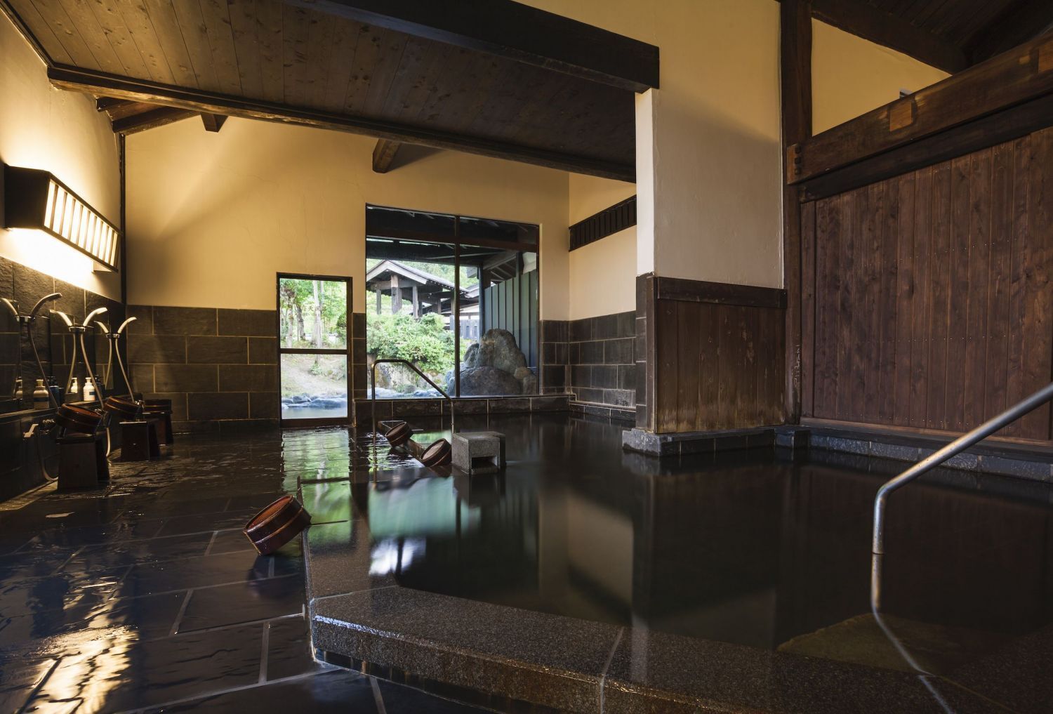 Un onsen japonés tradicional con suelo de piedra, interior de madera y vistas a un área boscosa.