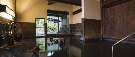 Un onsen japonés tradicional con suelo de piedra, interior de madera y vistas a un área boscosa.