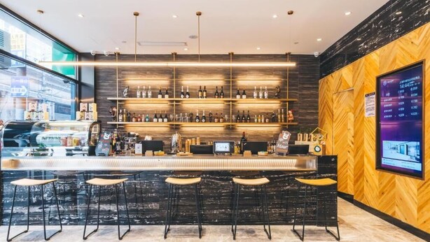 Zona de bar moderna amb paret de fusta i una pantalla digital que mostra informació.