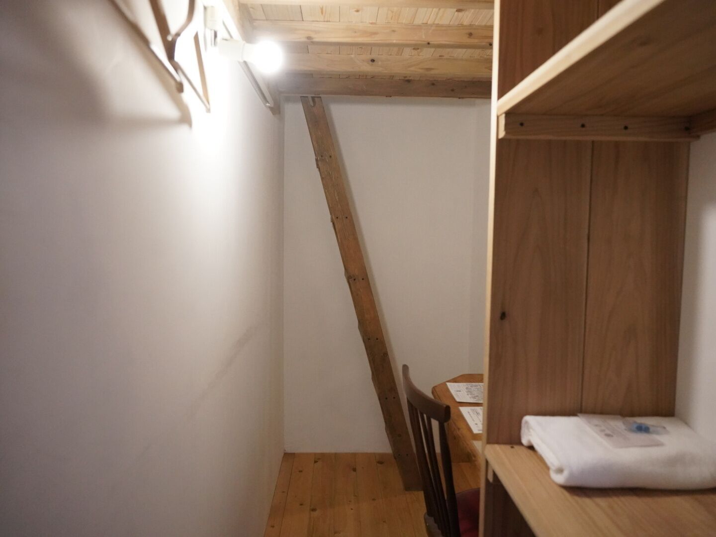 A narrow room with wooden beams on the ceiling, a wooden chair, and a small table with a folded white cloth.