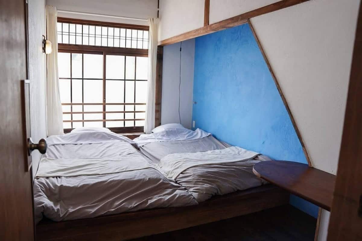 Een kamer met een bed, een raam met houten spijlen en een blauwe muur.