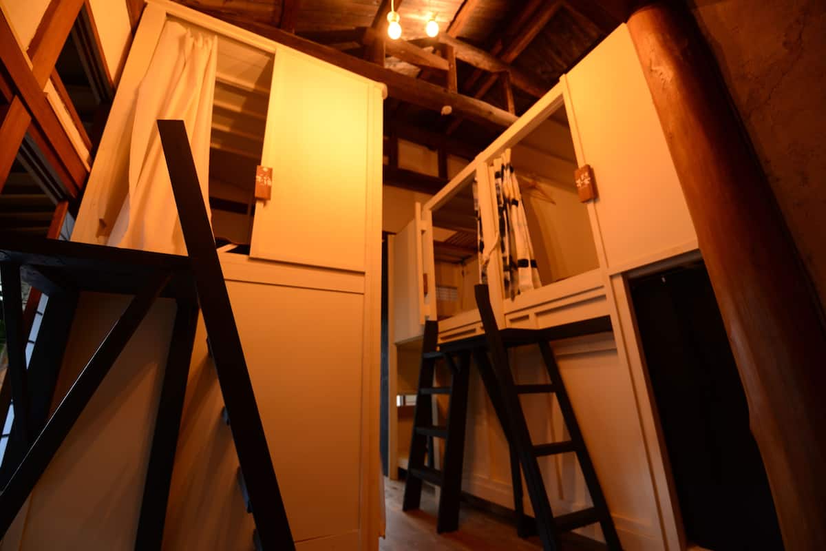 Een kamer met houten balken, een ladder en een raam met gordijnen.