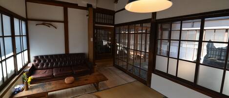 A traditional Japanese room with tatami flooring, a low wooden table, a cushioned bench, and a large window with wooden frames.