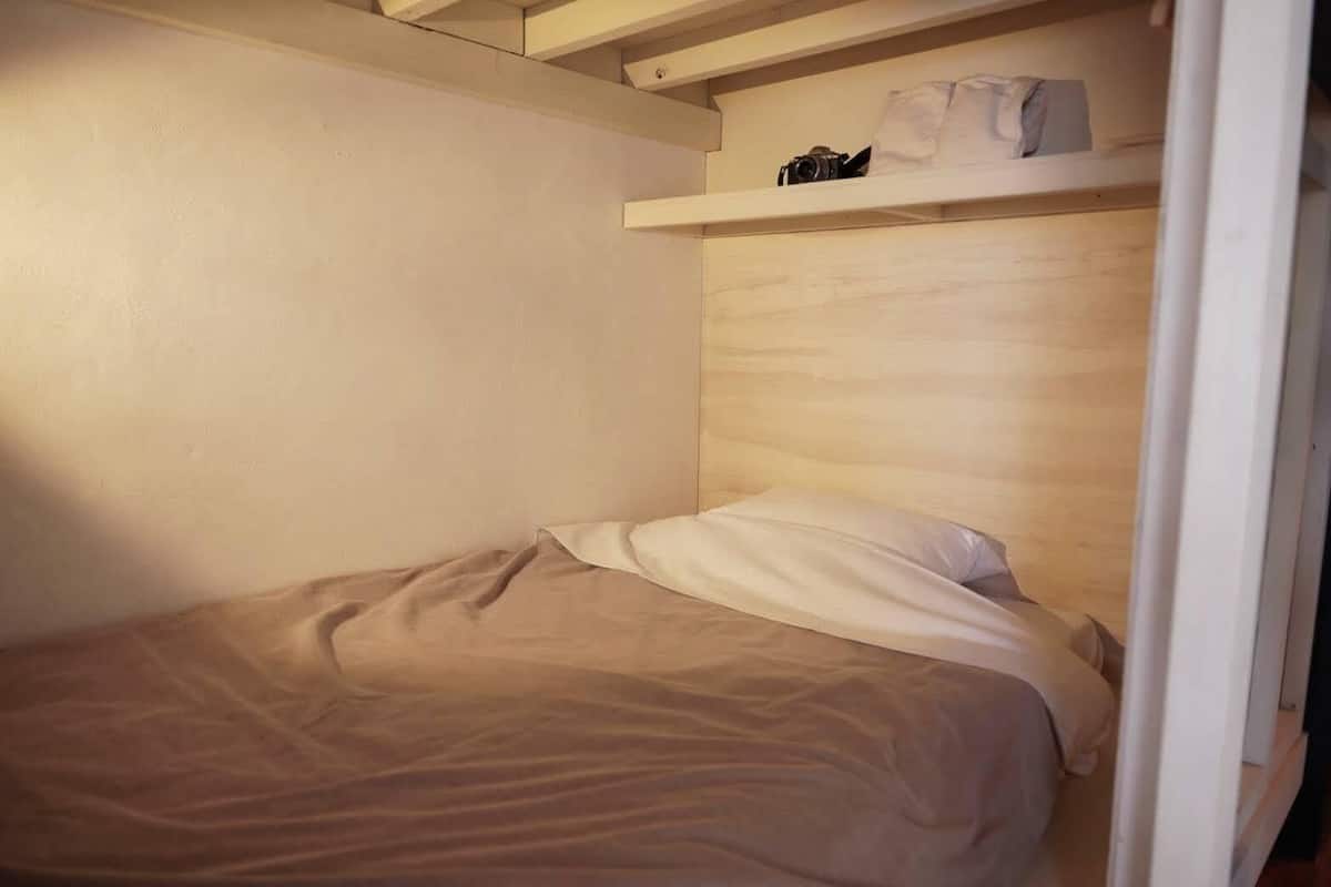 Een kleine kamer met een enkel bed, een houten hoofdbord en een plank boven het bed.