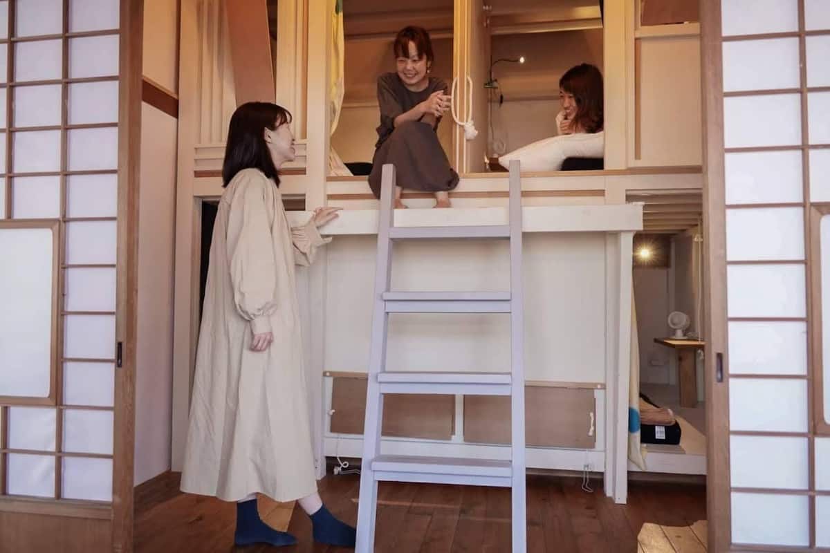 Een kamer met een houten vloer, een witte ladder en een persoon zittend op een plank.