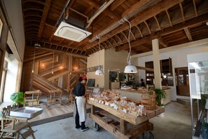 Une boulangerie avec des poutres en bois, une personne portant un tablier et du pain exposé en vitrine.