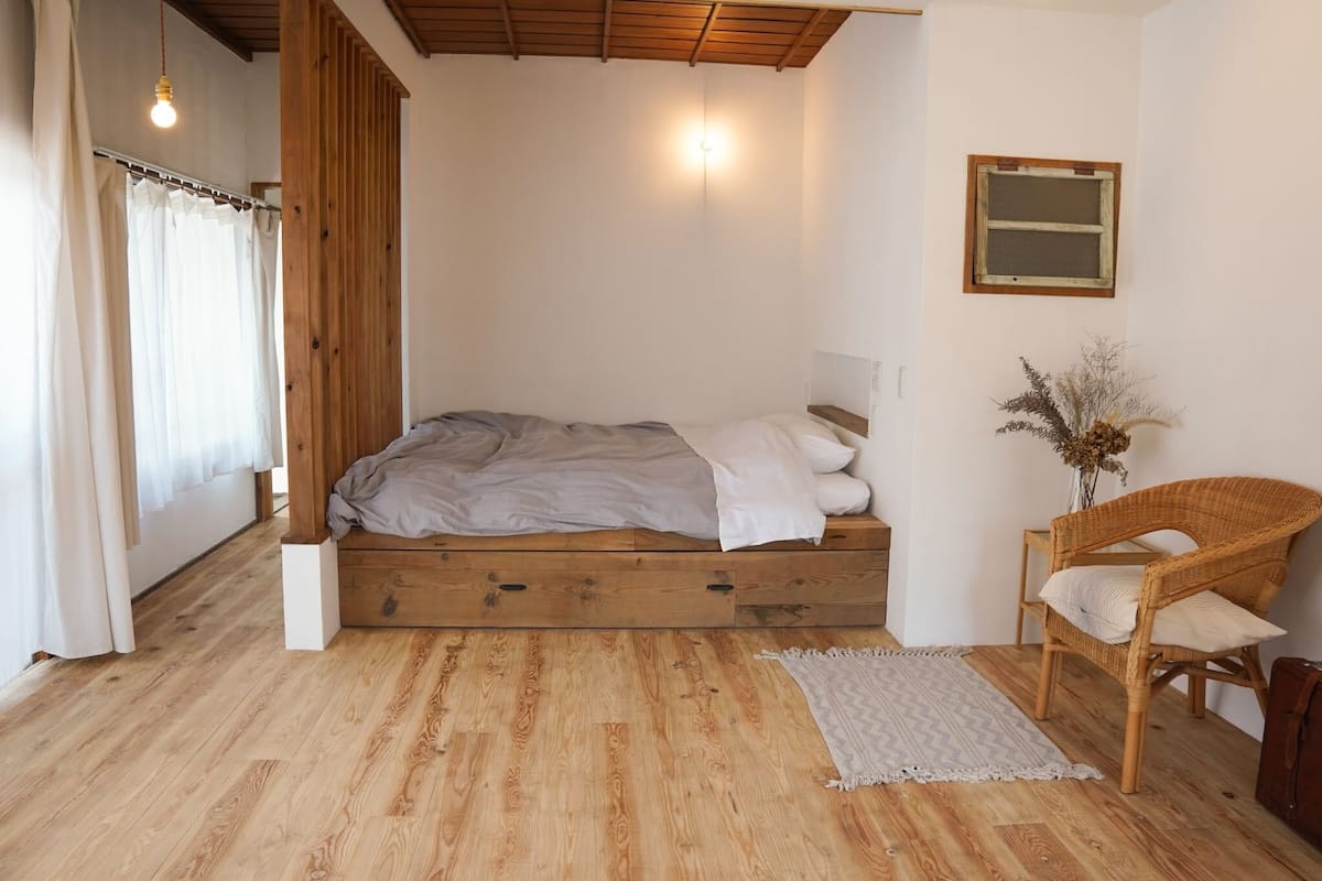 Een slaapkamer met een houten bed, een rieten stoel en een klein raam.
