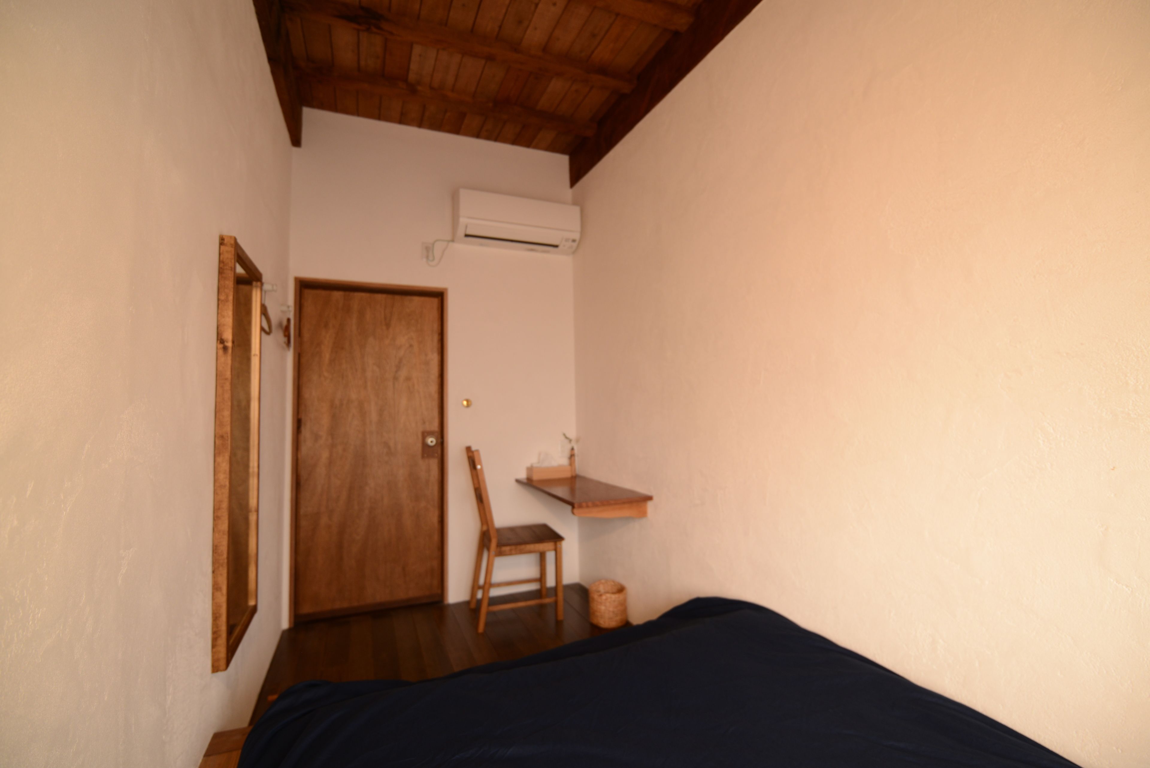 Una habitación pequeña y sencilla con una puerta de madera, una silla, una mesita y una cama.