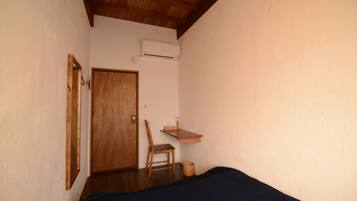 Una habitación pequeña y sencilla con una puerta de madera, una silla, una mesita y una cama.