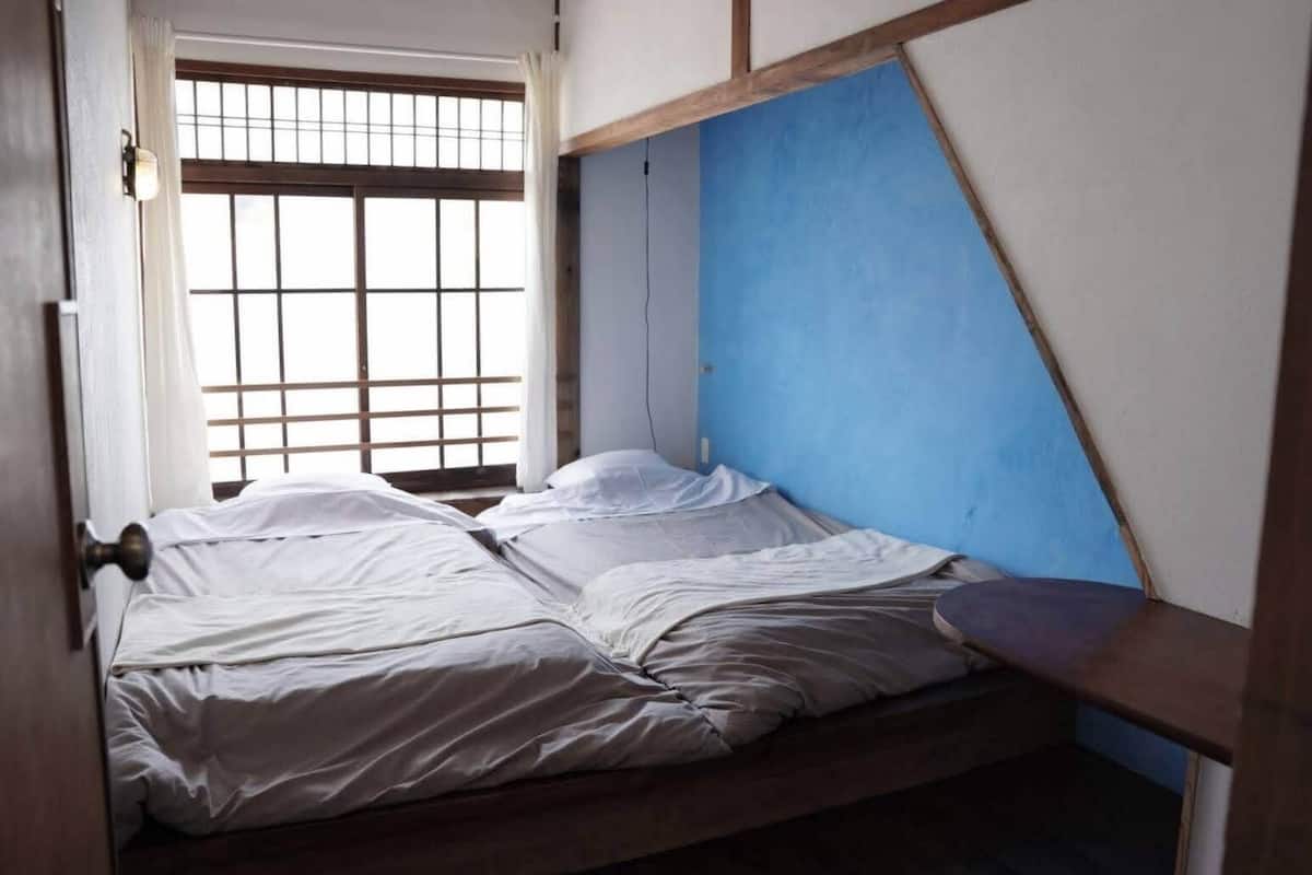 Een kamer met een bed, een raam met tralies en een blauwe wand.