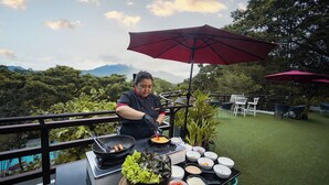 Um chef cozinha ao ar livre, com uma mesa repleta de ingredientes e utensílios.