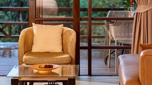 Uma área de estar aconchegante com sofá e poltrona, uma mesa de centro de vidro e vista para um deck exterior através de amplas janelas.