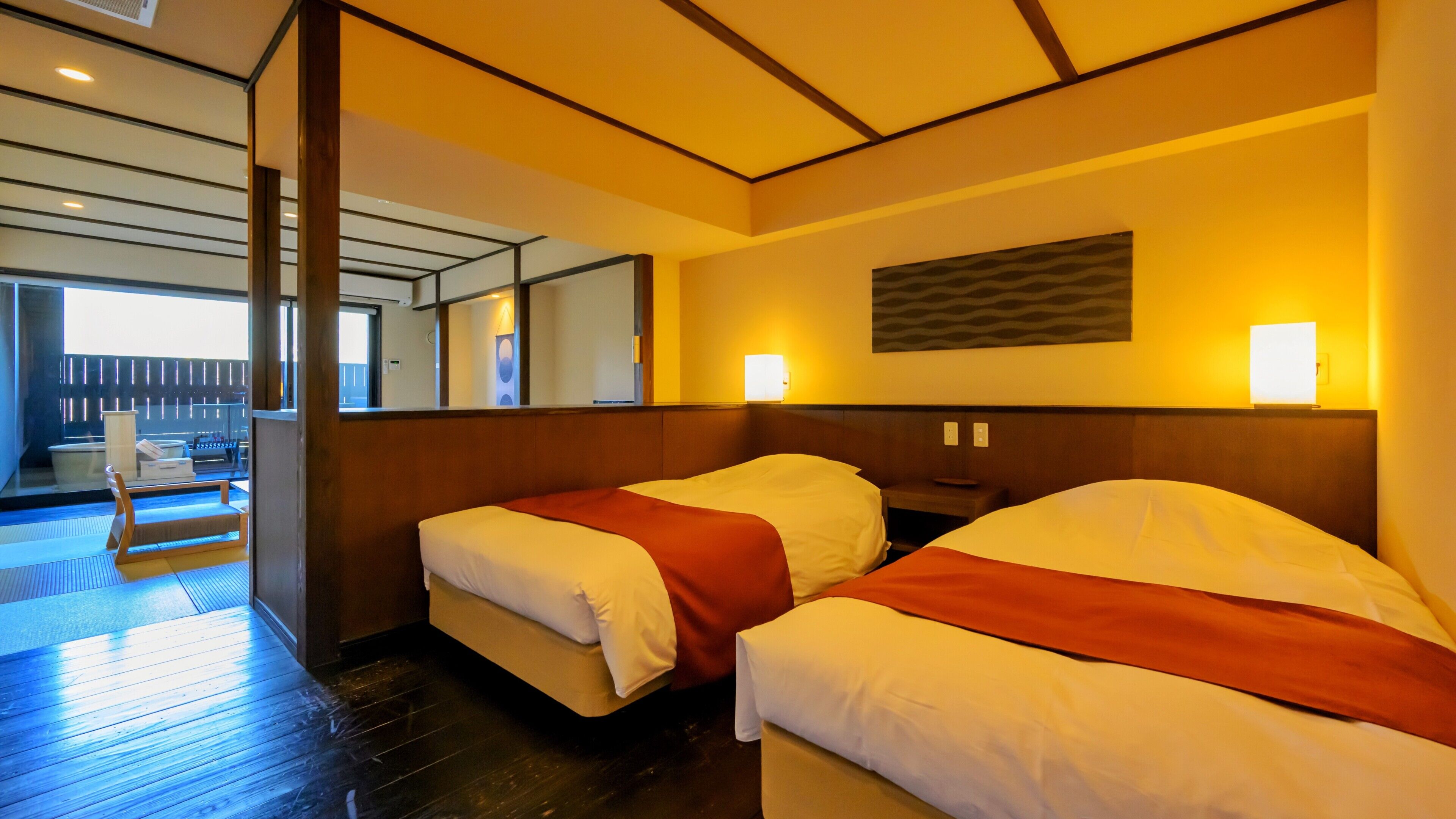A hotel room with two beds, a wooden floor, a large window, and a view of the outside.