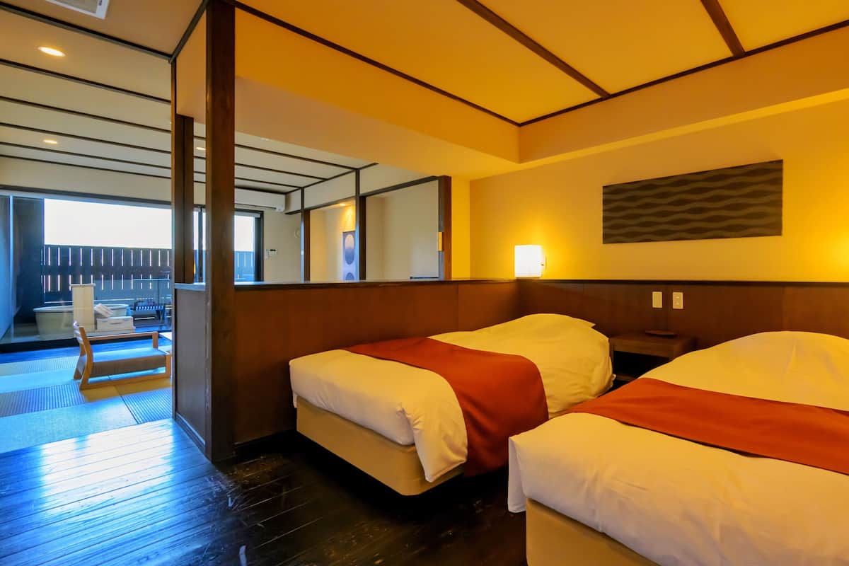 Habitación de hotel con dos camas, suelo de madera, un ventanal y vistas al exterior.