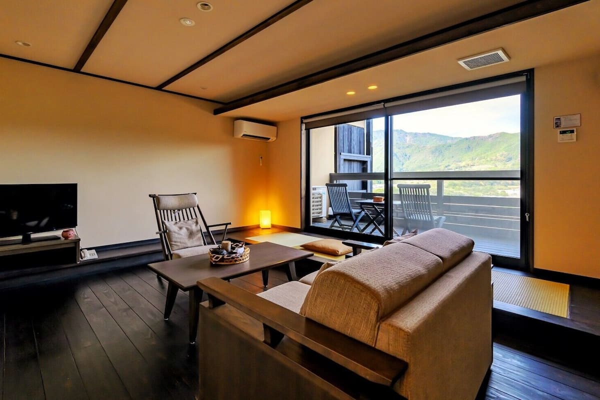 Una sala de estar moderna con un sofá, un televisor, una mesa con un objeto decorativo y un ventanal con vistas al exterior.