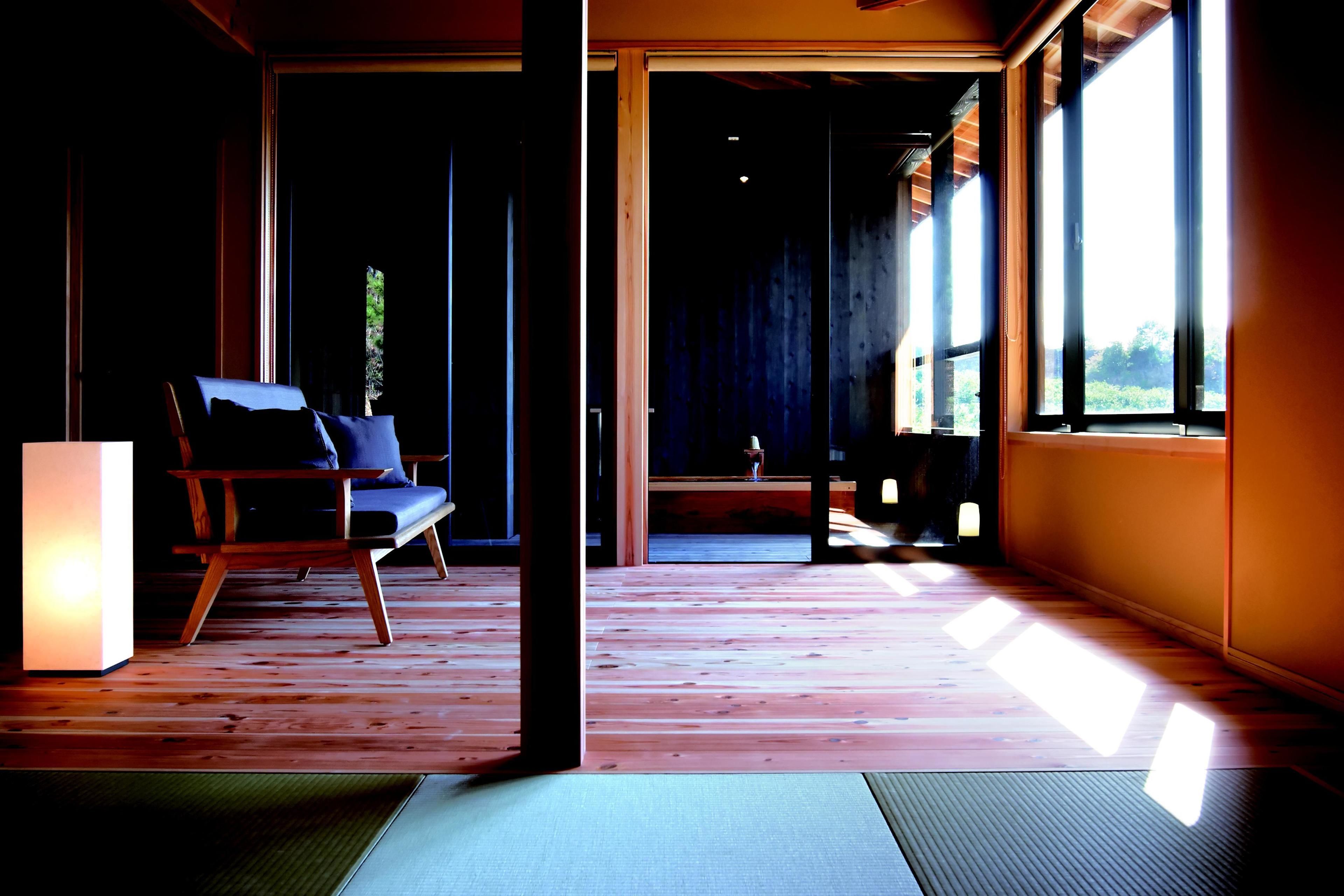 A room with a wooden floor, a chair, a table, and large windows allowing natural light.