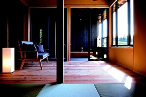 A room with a wooden floor, a chair, a table, and large windows allowing natural light.