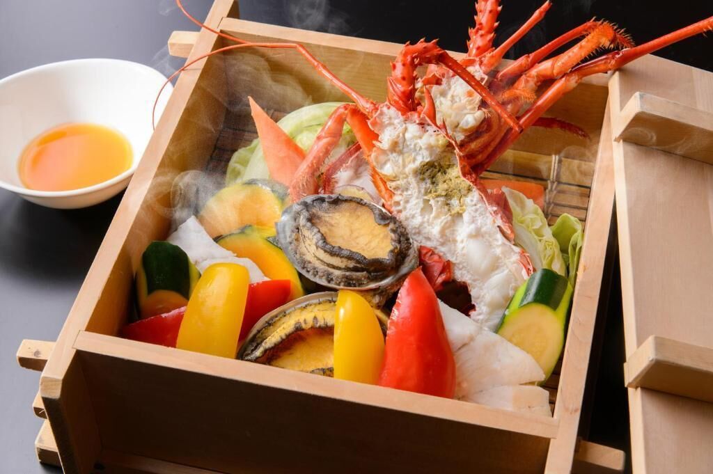 Una caja de madera con un langostino, diferentes verduras y un cuenco de salsa.