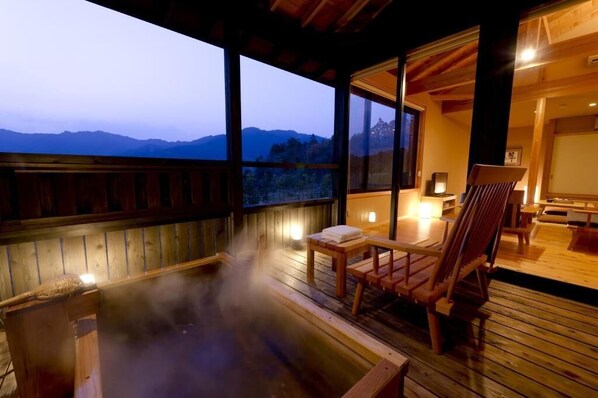 A wooden deck with a hot tub, wooden chairs, and a table with a lamp.