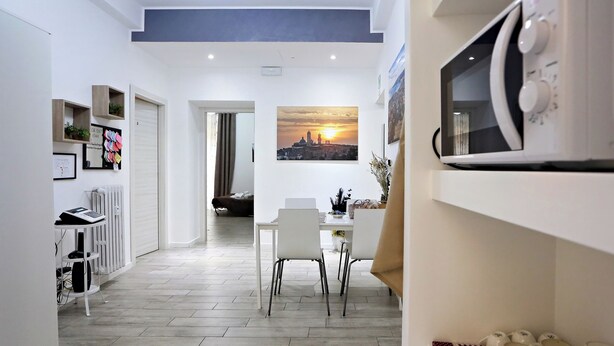 A modern kitchen with white cabinets, a dining area with a table and chairs, and a view of a sunset through a window. - Relais Villa Borghese (Rome)