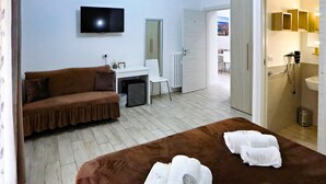 A hotel room with a brown sofa, a desk, a TV, and a bed with towels. - Relais Villa Borghese (Rome)