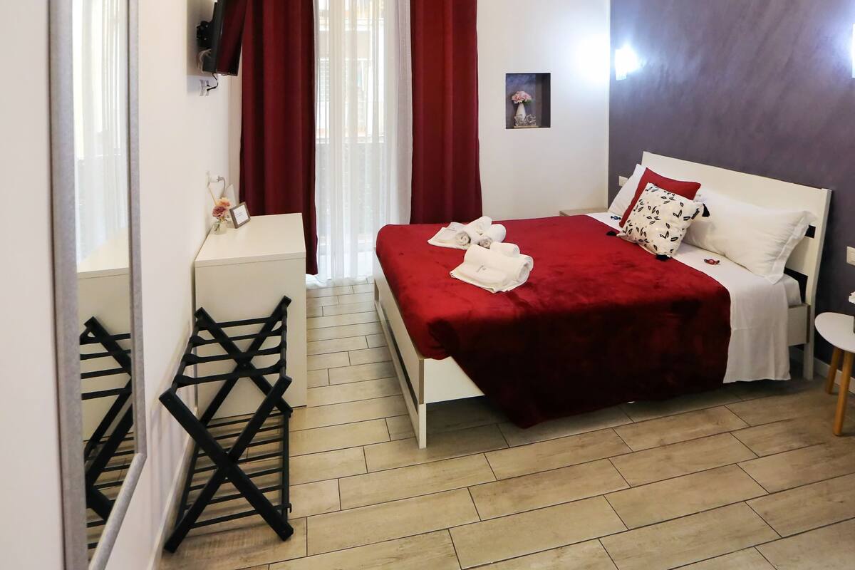 A hotel room with a bed, a desk, a chair, a mirror, and a small table.