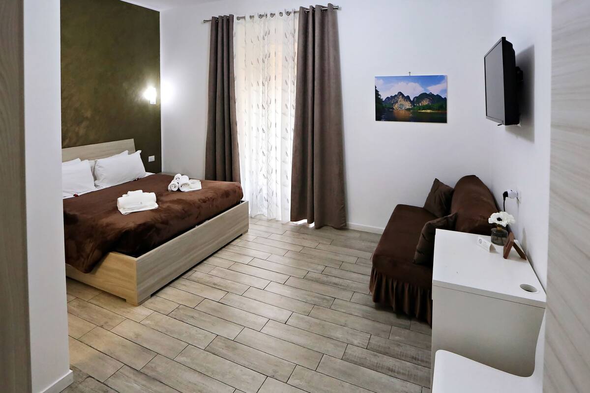 A hotel room with a bed, a desk, a chair, a TV, and a painting on the wall.