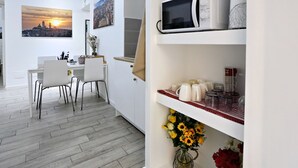 A modern kitchen with white cabinetry, a dining area with a white table and chairs, and a microwave on the countertop. - Relais Villa Borghese (Rome)