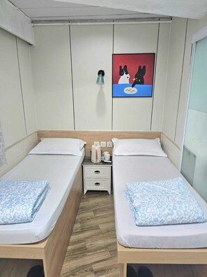 A twin room with two beds, a nightstand with a kettle, a wall clock, and a painting of dogs. - K&B Hostel (Kowloon)