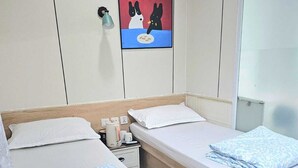 Dos camas individuales con estructura de madera, ropa de cama blanca, una mesita de noche con lámpara y un cuadro colgado en la pared.