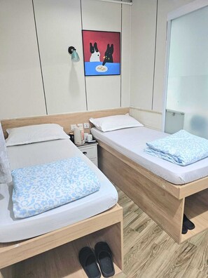 Two single beds with wooden frames, white bedding, a small bedside table with a lamp, and a wall-mounted artwork. - K&B Hostel (Kowloon)