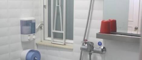 Un baño con inodoro, lavabo, ducha y ventana con marco de metal.