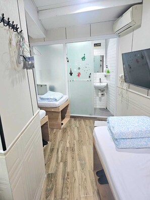 A compact hotel room with a bed, a small desk, a mirror, a television, and a bathroom with a sink and toilet. - K&B Hostel (Kowloon)