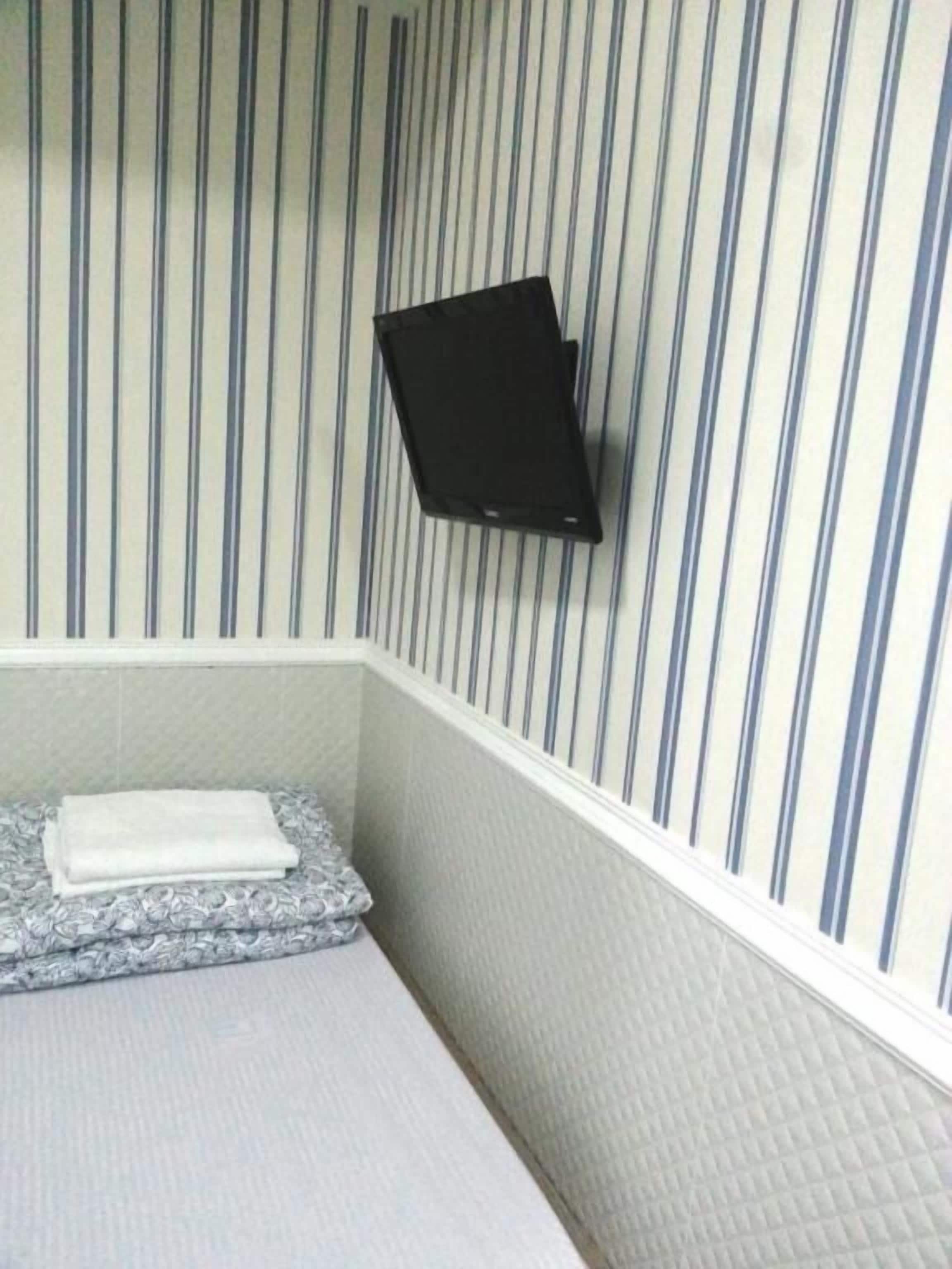 A bathroom with striped wallpaper, a black medicine cabinet, and a towel on a patterned mat.