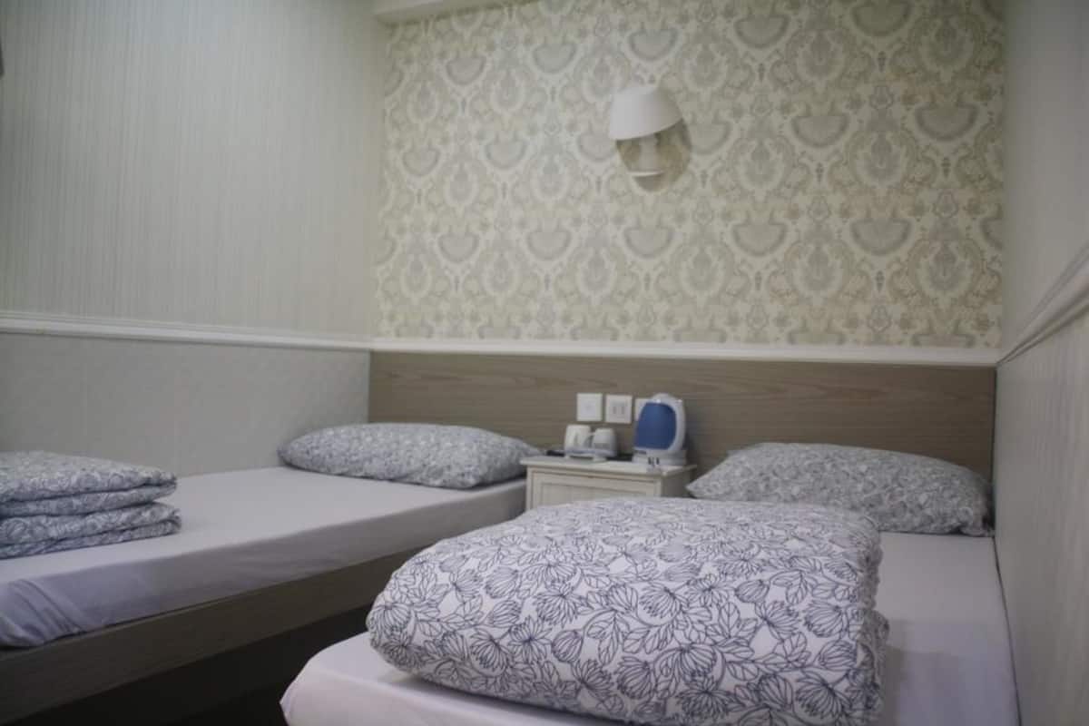 A hotel room with two beds, a nightstand, and a wall-mounted lamp.
