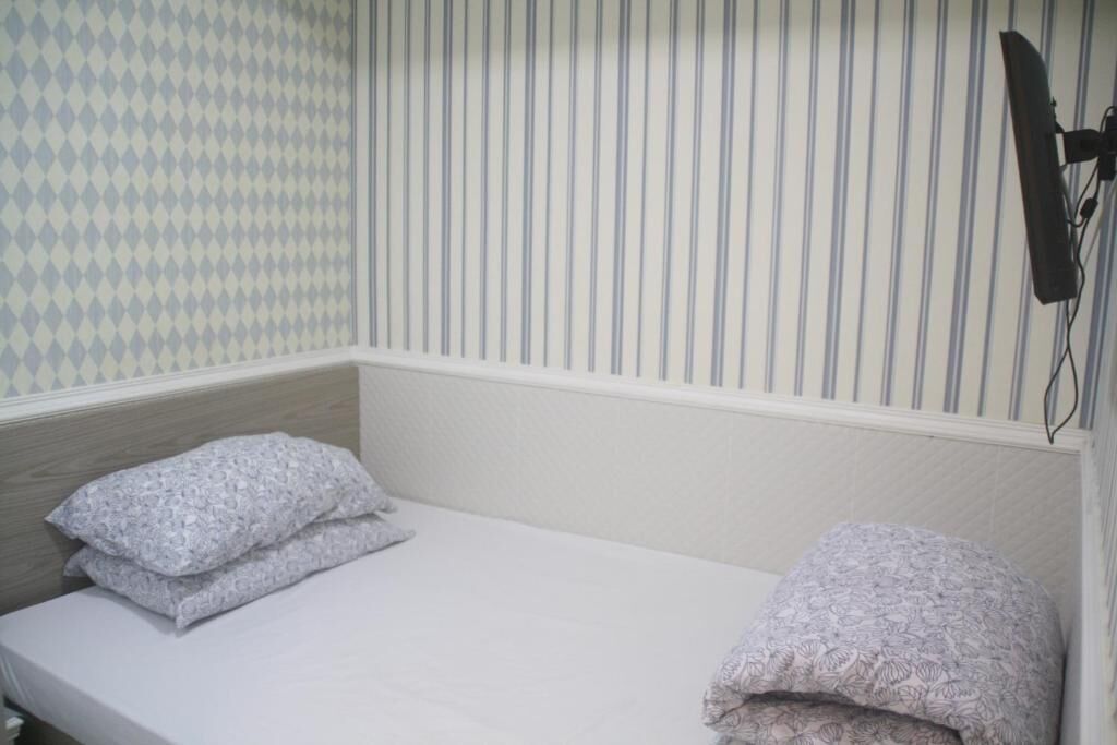 A small, single-bed room with a striped wallpaper pattern, a wooden headboard, and a wall-mounted telephone.