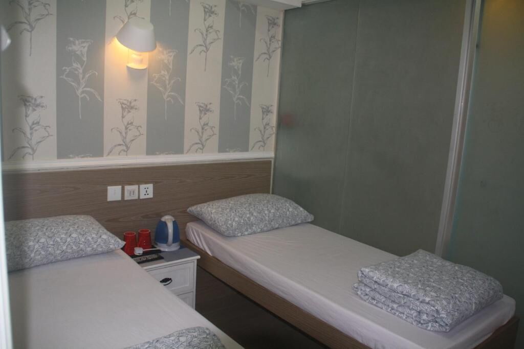 Habitación de hotel con dos camas individuales, una mesita de noche, una lámpara y una ventana con papel tapiz a rayas.