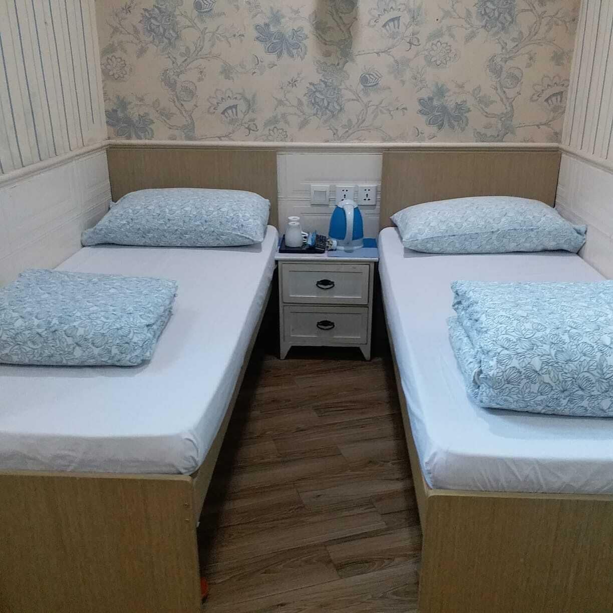Une chambre double avec deux lits simples, une table de chevet avec une bouilloire et une prise de courant.